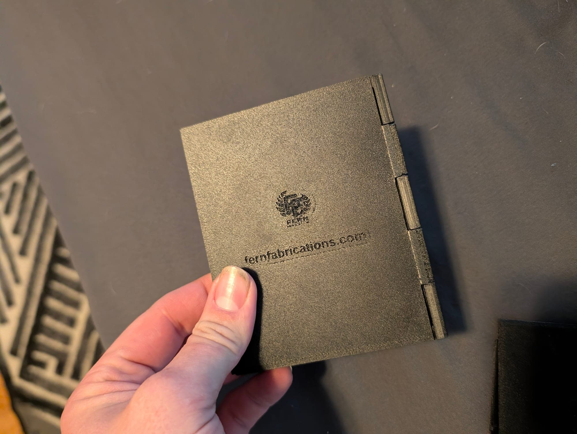 Closed card display case in olive, branded with the Fern Fabrications logo, held in one hand